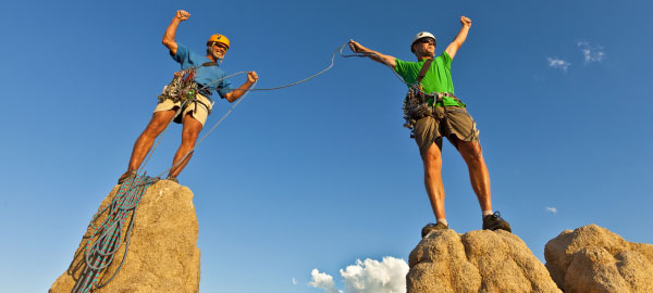 Team of 2 rock climbers with climbing ropes celebrate in victory pose after making it to the summit of rock pinnacles