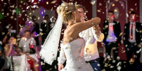 Bride and groom, showered by confetti whilst dancing at wedding reception venue whilst guests look on
